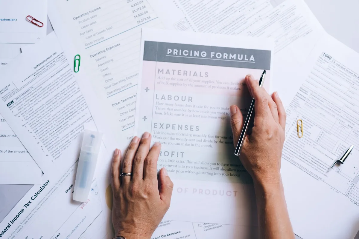 Hands organizing pricing documents and formula papers on a desk, representing the process of breaking down a tool’s true cost