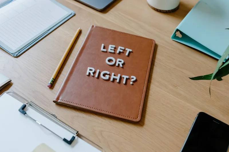 Notebook on a desk reading “Left or Right?” next to a pencil and clipboard